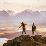Young couple of hikers with backpacks is walking at mountain top with great view